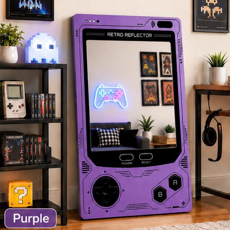 May include: A large purple floor mirror shaped like a handheld video game console. The frame features printed circuit board patterns, a directional pad, A and B buttons, and power and reset labels. The top displays the text RETRO REFLECTOR.