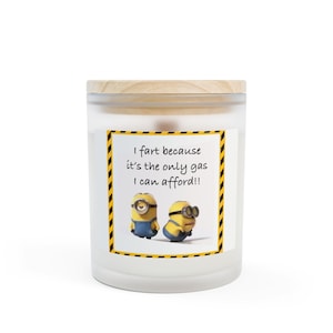 Op de afbeelding: Een witte kaars met een houten deksel. Het etiket bevat de tekst "I fart because it's the only gas I can afford!!" met cartoon Minion-personages. De kaars zit in een glazen pot.
