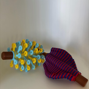 May include: Two colorful toys are displayed against a white background. One is a blue and yellow spiky ball with a brown handle. The other is a red and blue striped fabric object with a brown handle. Both toys appear to be made of plastic.