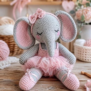 May include: A handmade crochet elephant doll in gray and pink, wearing a pink tutu, headband, and ballet slippers. The elephant has closed eyes and a sweet expression, perfect for a nursery or child's room.