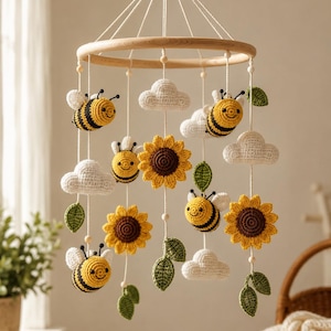 May include: A hanging mobile featuring crocheted elements suspended from a circular wooden frame. The mobile includes yellow and black striped bees, white clouds, yellow sunflowers with brown centers, and green leaves attached to white strings.