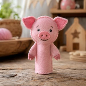 Puede incluir: Títere de cerdo rosa hecho a mano de fieltro, con una cara sonriente, ojos negros pequeños y orejas rosas. El cerdo tiene un cuerpo cilíndrico y brazos pequeños. El títere está diseñado para el juego y la narración de cuentos infantiles.