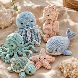 Può includere: Una collezione di creature marine all'uncinetto, tra cui un polpo, un cavalluccio marino, una balena, una stella marina e una tartaruga. I giocattoli sono nei toni del blu, rosa e verde, con occhi di sicurezza neri. Sono su sabbia.