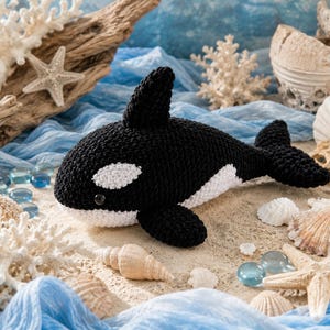 May include: A handcrafted crochet orca toy featuring a black body with a white underbelly and a distinct white patch near the eye. The plush marine animal has a prominent dorsal fin, side flippers, and a tail fluke, all worked in a textured yarn.