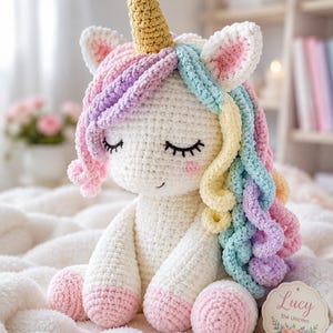 May include: A handmade crochet unicorn doll with a white body, pastel rainbow mane, and a golden horn. The unicorn has closed eyes and pink accents on its ears and hooves. A tag that says "Lucy the Unicorn" is attached.