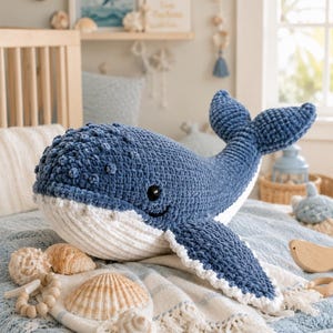 Puede incluir: Un juguete de peluche con forma de ballena hecho de hilo azul oscuro y blanco con una superficie de ganchillo texturizada. La ballena presenta una cabeza redondeada con pequeños bultos, una parte inferior blanca con estrías y un ojo.