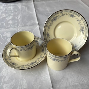 Op de afbeelding: Een crèmekleurige theeservies met blauwe bloemmotieven en zilveren rand. De set bestaat uit twee kopjes en twee schotels, met een extra schotel op de achtergrond. De kopjes hebben een klassiek oor. Voor thee of koffie.