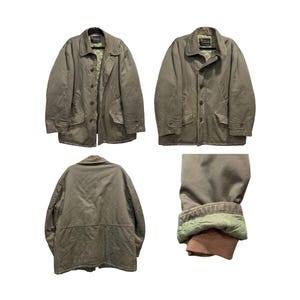 May include: A taupe-coloured utility jacket featuring a collared neckline, a button-front closure, and two front flap pockets. The interior is lined with a light green quilted fabric, and the sleeves include ribbed brown cuffs at the wrists.