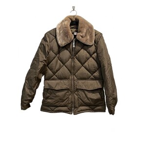 May include: A quilted olive green jacket featuring a diamond-patterned stitch, a full-length front zipper, and two large flap pockets at the waist. The jacket includes a wide, plush tan faux fur collar and long sleeves with simple cuffs.