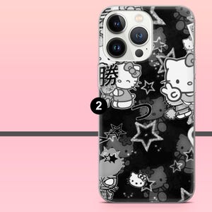 Puede incluir: Funda de tel&eacute;fono en blanco y negro con un patr&oacute;n repetido de personajes de Hello Kitty, estrellas y texto japon&eacute;s. La funda tiene un borde transparente y un fondo negro. El n&uacute;mero "2" es visible en la funda.