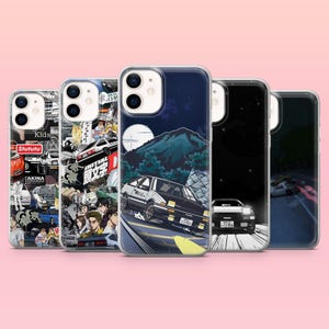 Puede incluir: Cinco fundas transparentes para smartphone con varios diseños gráficos inspirados en la serie de anime Initial D. Los diseños incluyen collages de personajes y coches, un coche blanco y negro en una carretera de montaña de noche y un coche.