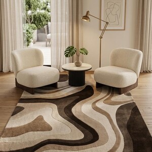 May include: A rectangular area rug featuring a multi-tonal abstract pattern of flowing, organic shapes in shades of cream, beige, and dark brown. The rug has a plush, textured surface and is positioned beneath two cream-colored armchairs.