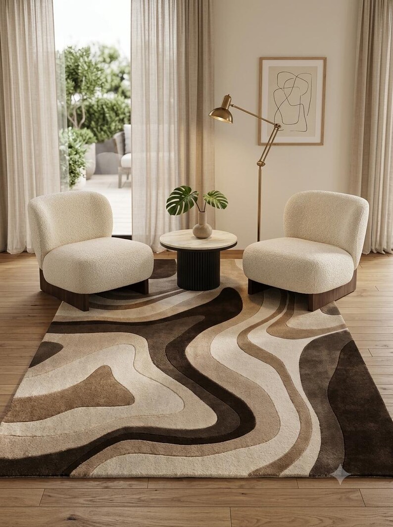 May include: A rectangular area rug featuring a multi-tonal abstract pattern of flowing, organic shapes in shades of cream, beige, and dark brown. The rug has a plush, textured surface and is positioned beneath two cream-colored armchairs.