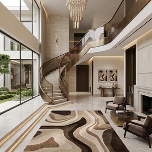 May include: A rectangular area rug featuring a flowing, abstract pattern of layered wavy lines in shades of dark brown, tan, and cream. The rug is positioned on a polished light-colored stone floor in a spacious, multi-level interior entryway.
