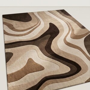 May include: A rectangular area rug featuring a layered, wavy pattern in shades of dark brown, medium brown, beige, and cream. The design consists of fluid, organic shapes that create a sense of depth and movement across the entire surface of the rug.