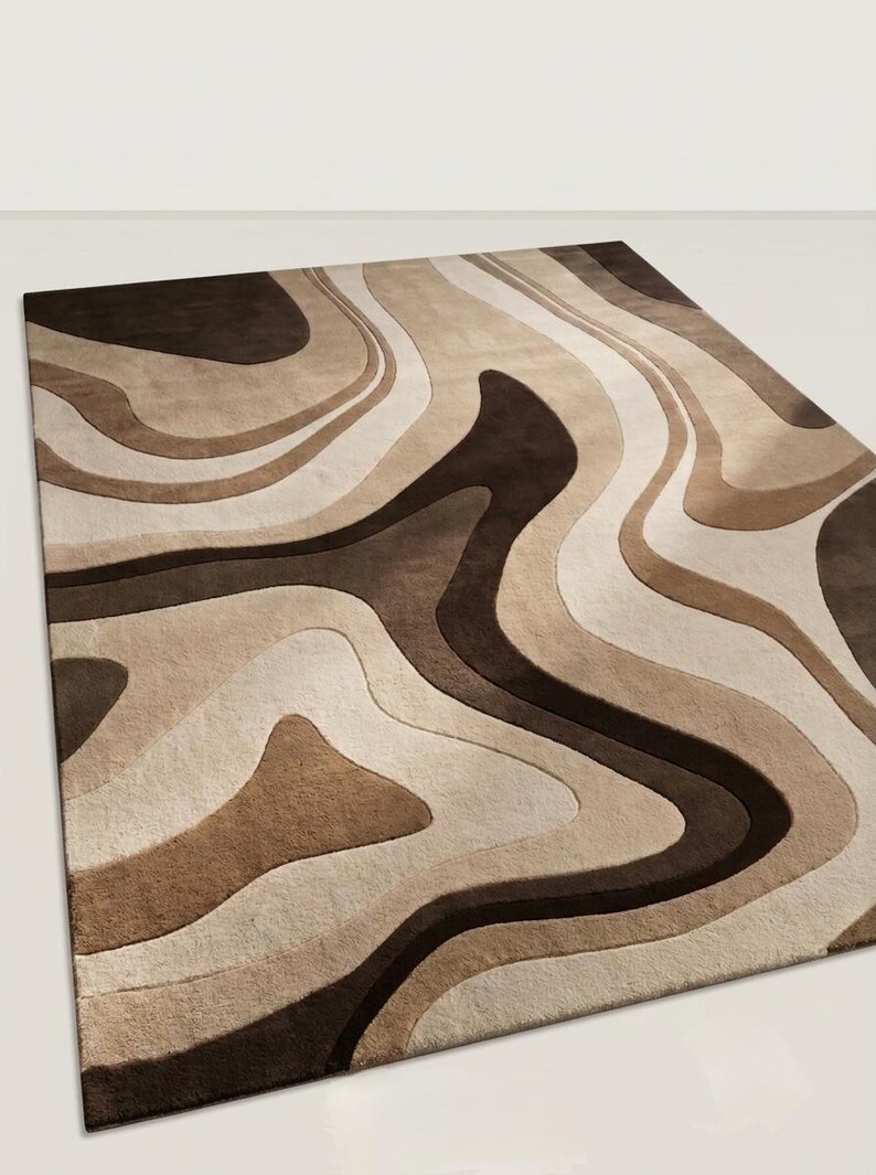 May include: A rectangular area rug featuring a layered, wavy pattern in shades of dark brown, medium brown, beige, and cream. The design consists of fluid, organic shapes that create a sense of depth and movement across the entire surface of the rug.