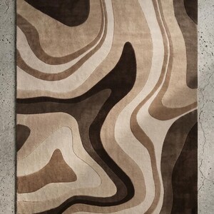 May include: A rectangular area rug featuring a layered, abstract pattern of flowing, organic shapes. The design consists of varying shades of dark brown, medium tan, and cream, creating a fluid, topographic-like aesthetic across the surface.