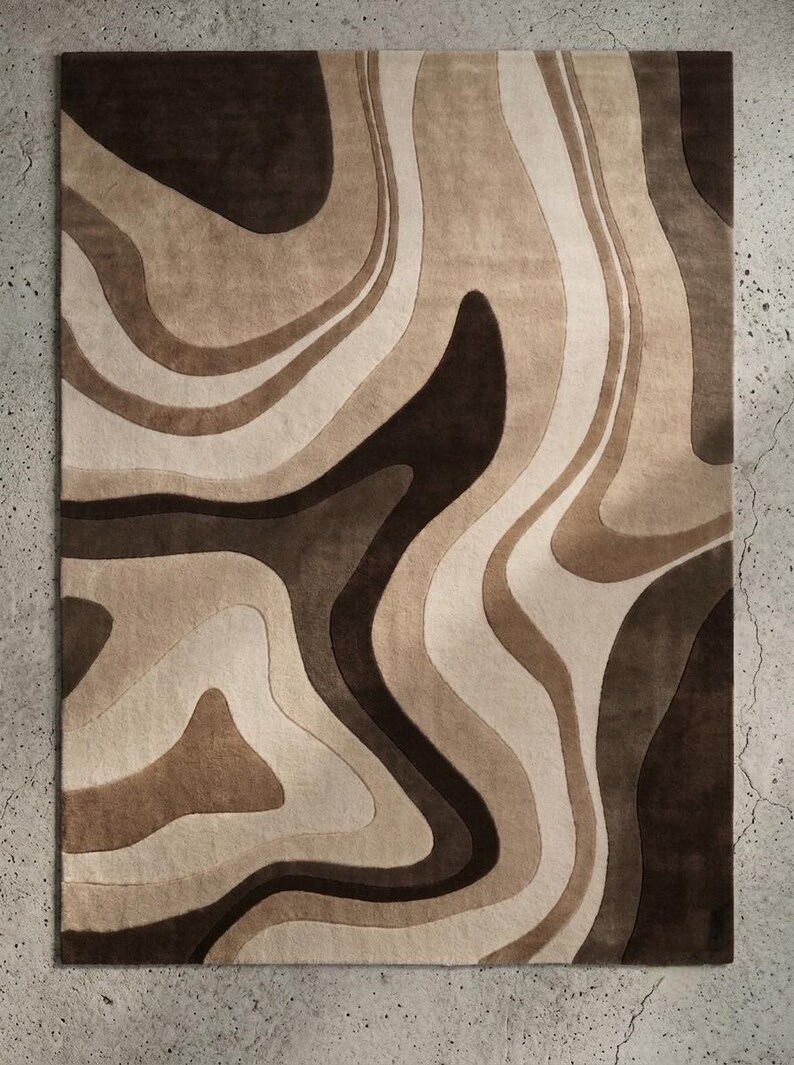 May include: A rectangular area rug featuring a layered, abstract pattern of flowing, organic shapes. The design consists of varying shades of dark brown, medium tan, and cream, creating a fluid, topographic-like aesthetic across the surface.