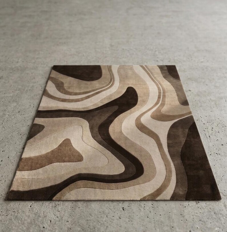 May include: A rectangular area rug featuring a fluid, abstract pattern of swirling organic shapes. The design consists of layered, wavy bands in varying shades of dark brown, medium brown, tan, and cream, creating a topographic effect.