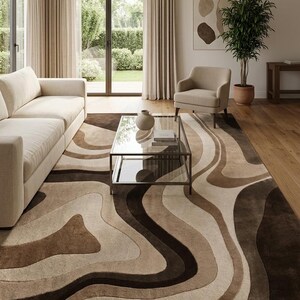 May include: A large rectangular area rug featuring a flowing, organic pattern of wavy, layered bands in shades of cream, beige, tan, and dark chocolate brown. The rug has a soft, textured pile and covers a significant portion of the wooden floor.
