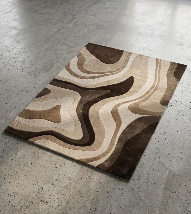 May include: A rectangular area rug featuring a layered, wavy pattern in various shades of brown, tan, and cream. The design consists of fluid, organic shapes that create a sense of depth and movement across the surface of the floor covering.