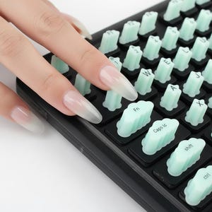 May include: Close-up of a black mechanical keyboard with mint green keycaps. The keycaps have white lettering and symbols. The keyboard is partially obscured by a hand with long, clear fingernails.