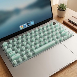 May include: A light mint green silicone keyboard cover featuring raised, cloud-shaped keys with printed black letters and symbols. The cover is placed over the keys of a silver laptop, providing a textured, tactile surface for typing.
