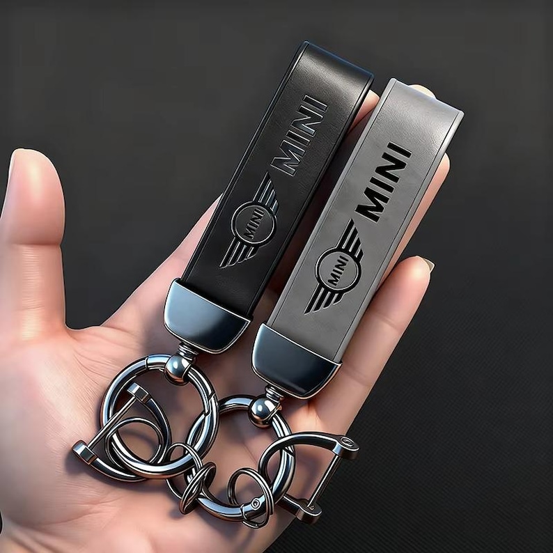 May include: Two leather keychains, one black and one gray, featuring the word "MINI" and a winged emblem. The keychains have silver-colored metal hardware, including key rings and a clasp.