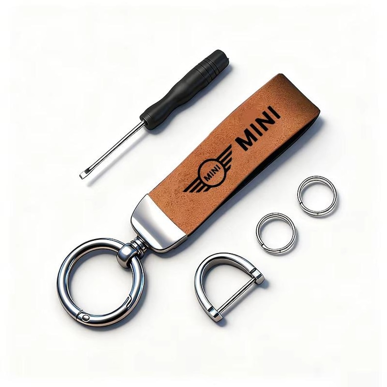 May include: A brown leather keychain strap with the "MINI" logo and text, a silver key ring, two small silver rings, a silver D-ring, and a black screwdriver. The keychain is designed for car keys.