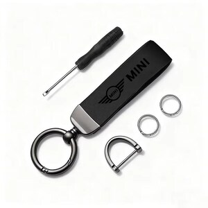 May include: Black leather keychain with the "MINI" logo and a small screwdriver. Includes two key rings and a D-ring. The keychain has a metal clasp and a black strap. The MINI logo is embossed on the strap.