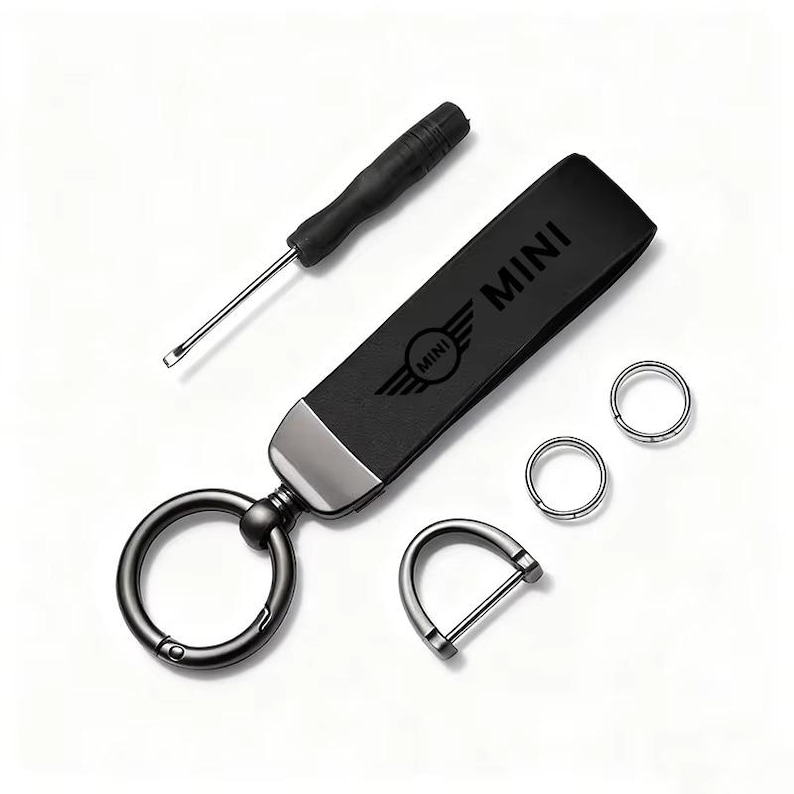 May include: Black leather keychain with the "MINI" logo and a small screwdriver. Includes two key rings and a D-ring. The keychain has a metal clasp and a black strap. The MINI logo is embossed on the strap.