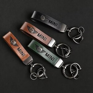 May include: Four leather keychains in black, brown, tan, and green. Each keychain has the word "MINI" printed on it, along with the MINI logo. The keychains have a silver metal ring attached.