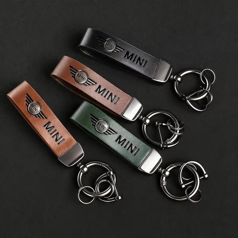 May include: Four leather keychains in black, brown, tan, and green. Each keychain has the word "MINI" printed on it, along with the MINI logo. The keychains have a silver metal ring attached.