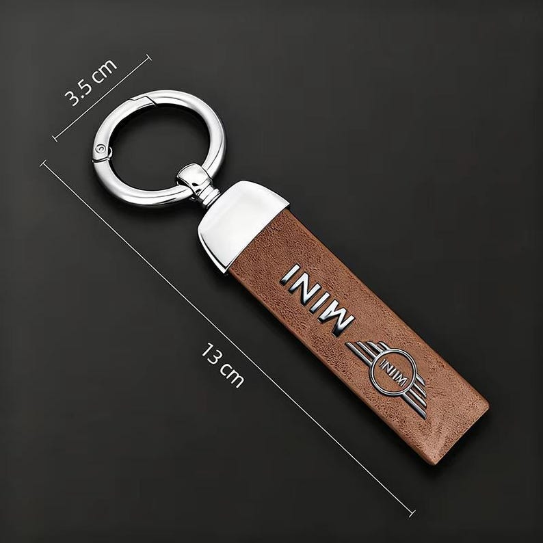 May include: A brown leather keychain with a silver metal ring and accents. The keychain is 5.1 inches long and 1.4 inches wide, with the word "MINI" and a logo embossed on the front.