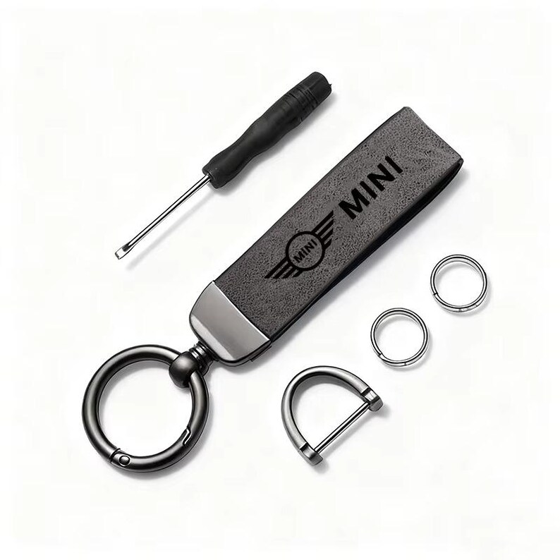 May include: A black leather keychain with the word "MINI" and the MINI logo. Includes a small screwdriver, two key rings, and a D-ring. The keychain is dark gray with a silver-colored metal accent.