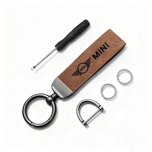 May include: A brown leather keychain with the word "MINI" and logo, a black screwdriver, and silver key rings. The keychain has a metal clasp and a D-ring. The items are arranged on a white surface.
