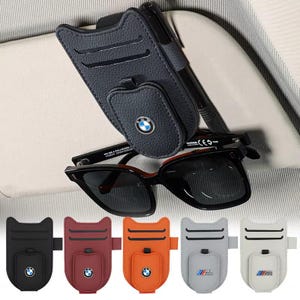 May include: A black leather car visor organiser with a BMW logo, holding sunglasses and a pen. Below are four additional organisers in black, burgundy, orange, grey, and white, each with a BMW or M logo.