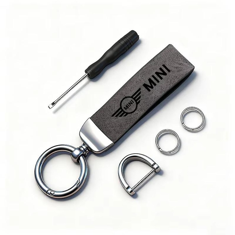 May include: A gray leather keychain with the word "MINI" and the MINI logo, a screwdriver, and several metal rings. The keychain has a silver metal clasp and a D-ring. The items are on a white background.