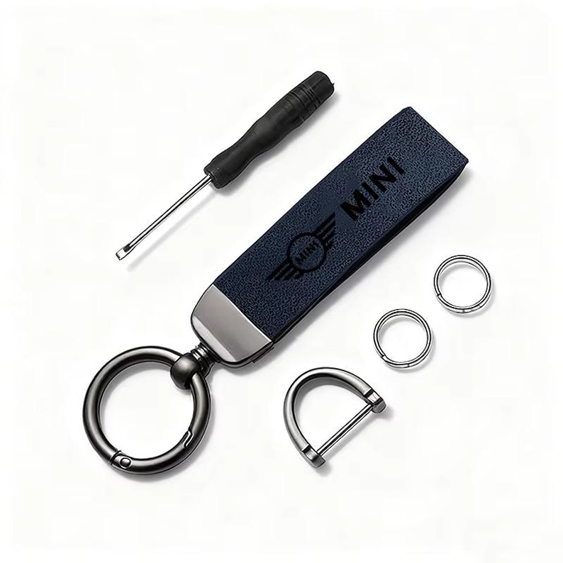 May include: A navy blue leather keychain with the word "MINI" and logo, a small screwdriver, and two silver key rings. The keychain has a silver metal accent and a large, black metal key ring. Additional silver metal D-ring is also included.