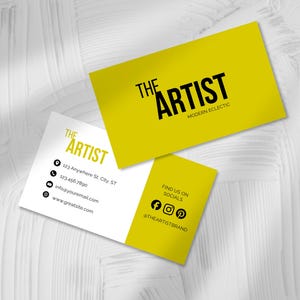 May include: Two rectangular business cards featuring a mustard yellow and white colour scheme. One card displays the black text THE ARTIST MODERN ECLECTIC. The other card shows contact details, social media icons, and the handle @THEARTISTBRAND.