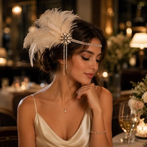 May include: A headpiece featuring a cream-colored feather plume attached to a circular crystal brooch. Two thin, sparkling crystal-encrusted bands wrap around the head, with two delicate crystal fringe strands hanging down from the side.