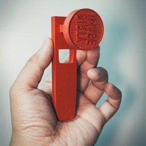 Peut inclure: Un tampon rouge avec le texte "IMAGE DIRTY" sur une surface circulaire. Le tampon est tenu dans une main et possède une poignée rectangulaire avec une découpe carrée. Le tampon est fait d'un matériau solide.