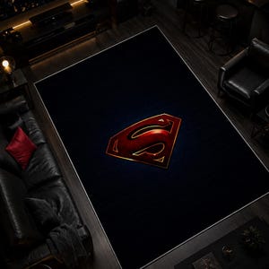 Può includere: Un grande tappeto rettangolare nero con un bordo bianco. Il tappeto presenta il logo di Superman in rosso e oro al centro. Il tappeto si trova in un soggiorno con mobili neri e pavimento in legno scuro.