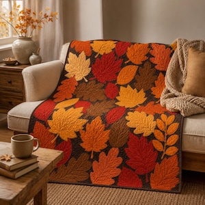 May include: A quilted throw blanket featuring a repeating pattern of autumn leaves in shades of red, orange, yellow, and brown. The fabric displays intricate stitching details that outline the shapes of various maple and oak leaves across the surface.