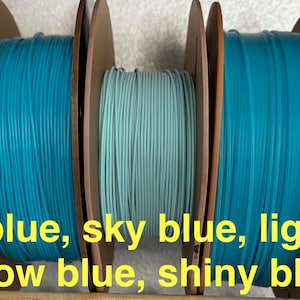 May include: Spools of 3D printing filament in various shades of blue, including royal blue, sky blue, light blue, glow blue, and shiny blue. The spools are mounted on brown cardboard reels.