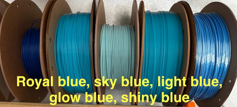 May include: Spools of 3D printing filament in various shades of blue, including royal blue, sky blue, light blue, glow blue, and shiny blue. The spools are mounted on brown cardboard reels.