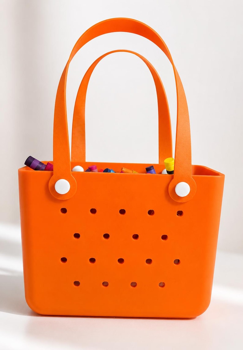 May include: Bright orange tote bag with two arched handles and a series of small holes on the front. The bag is filled with colorful items. White circular fasteners secure the handles to the bag.