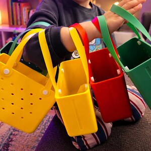 May include: A collection of colorful tote bags in yellow, yellow, red, and green. The bags have handles and are held together. The yellow bag has multiple holes. The bags are made of a durable material.