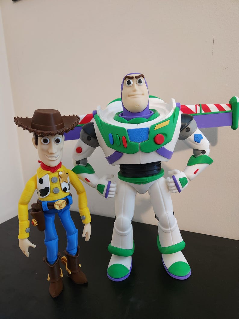 May include: A plastic action figure of a cowboy wearing a brown hat, yellow shirt, and blue trousers standing next to a plastic action figure of a space ranger with a purple hood, white and green suit, and retractable wings with red and white stripes.