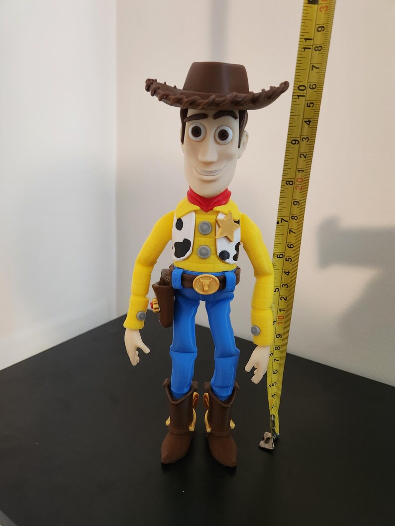 May include: A Sheriff Woody action figure wearing a brown cowboy hat, yellow long-sleeve shirt with black and white cow print vest, red neckerchief, blue trousers, and brown boots. A yellow measuring tape shows the figure is approximately 30 cm tall.